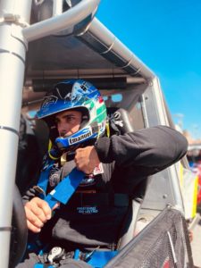 Emanuel Costa in vehicle, in full racing gear, adjusting seatbelt